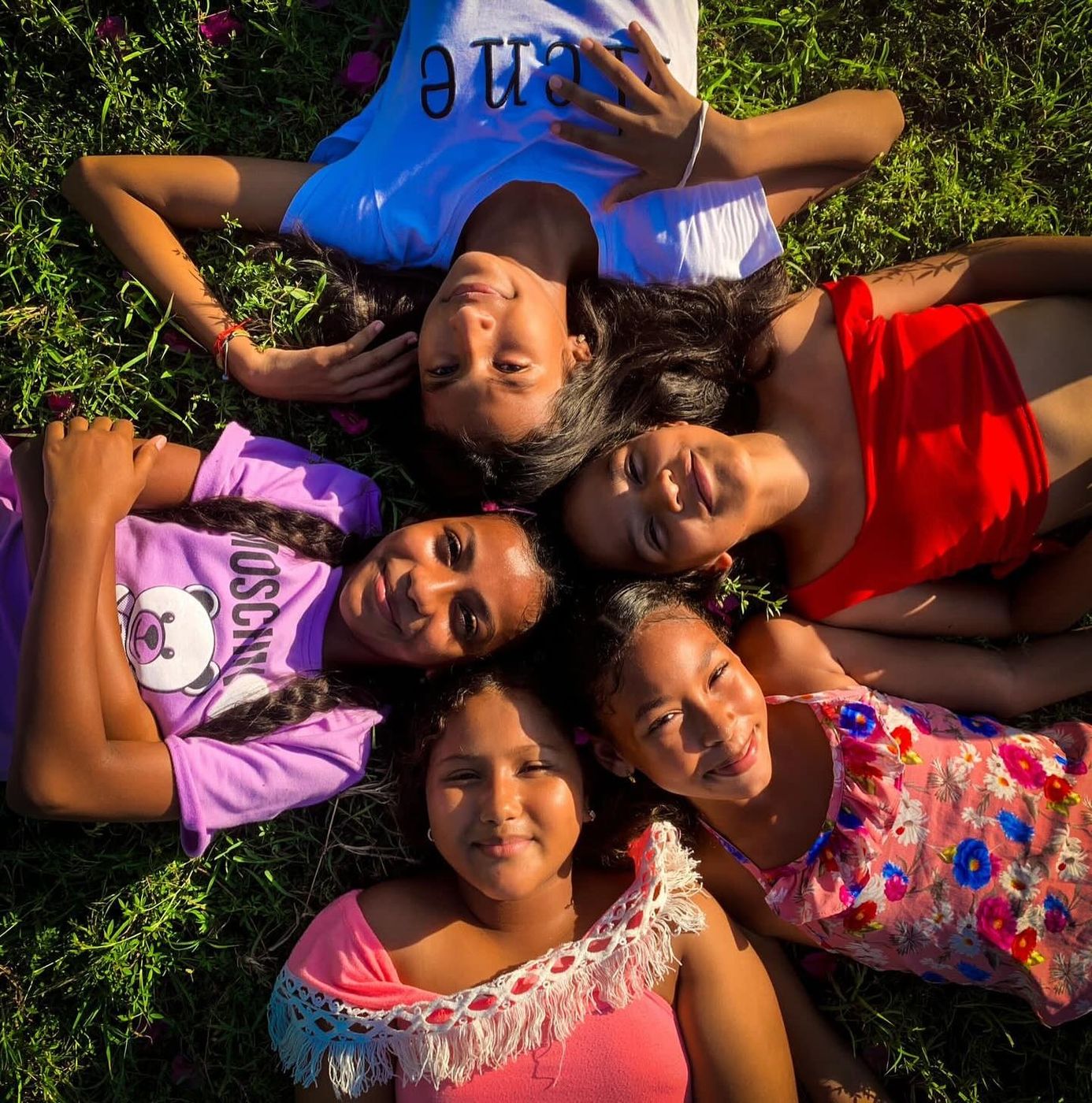 Cinco niñas de Somos Arte sonriendo, acostadas en círculo sobre el pasto